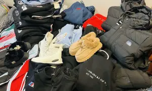 Stos ubrań i butów: czarne kurtki, bluzy, białe buty zimowe, kapcie futrzane i beżowe botki.