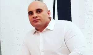 Dominik Abus, wiek nieznany, w białej koszuli, na tle białej ściany z czarnymi pasami.