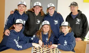 Grupa osób w bluzach i czapkach z logo "TuRa Chess" gra w szachy.