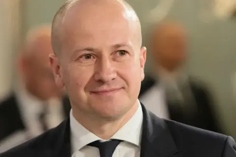Uśmiechnięty mężczyzna w garniturze, być może partner popularnej aktorki, który zrezygnował z kariery dla niej.