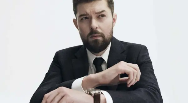 Mężczyzna w garniturze, z zarostem, zastanawia się, czy Remigiusz Mróz ma żonę.