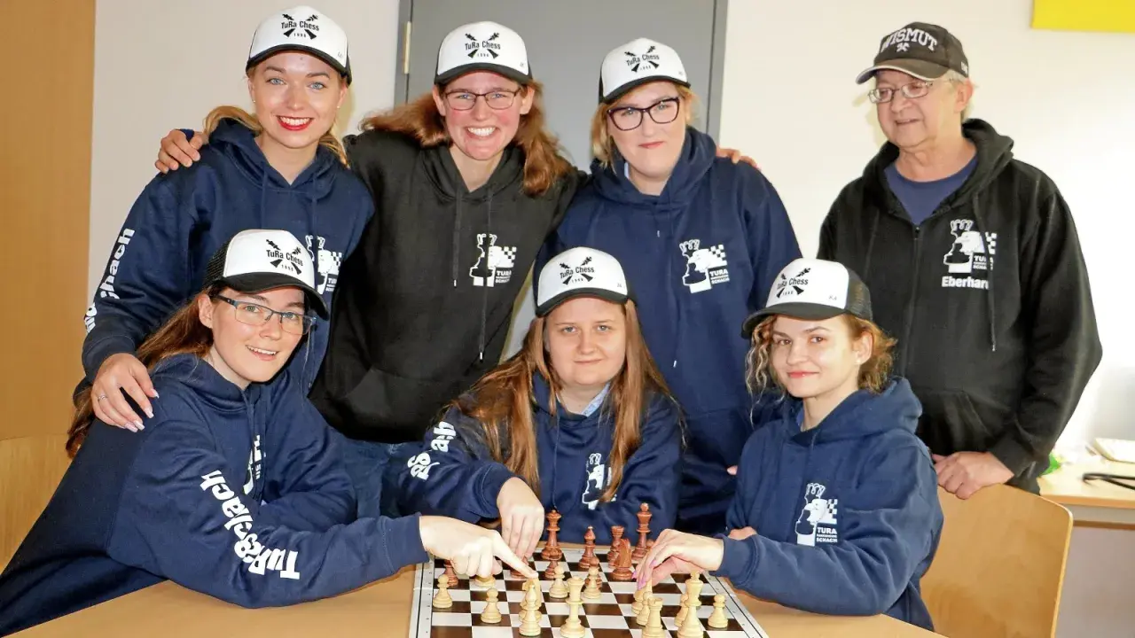 Grupa osób w bluzach i czapkach z logo "TuRa Chess" gra w szachy.