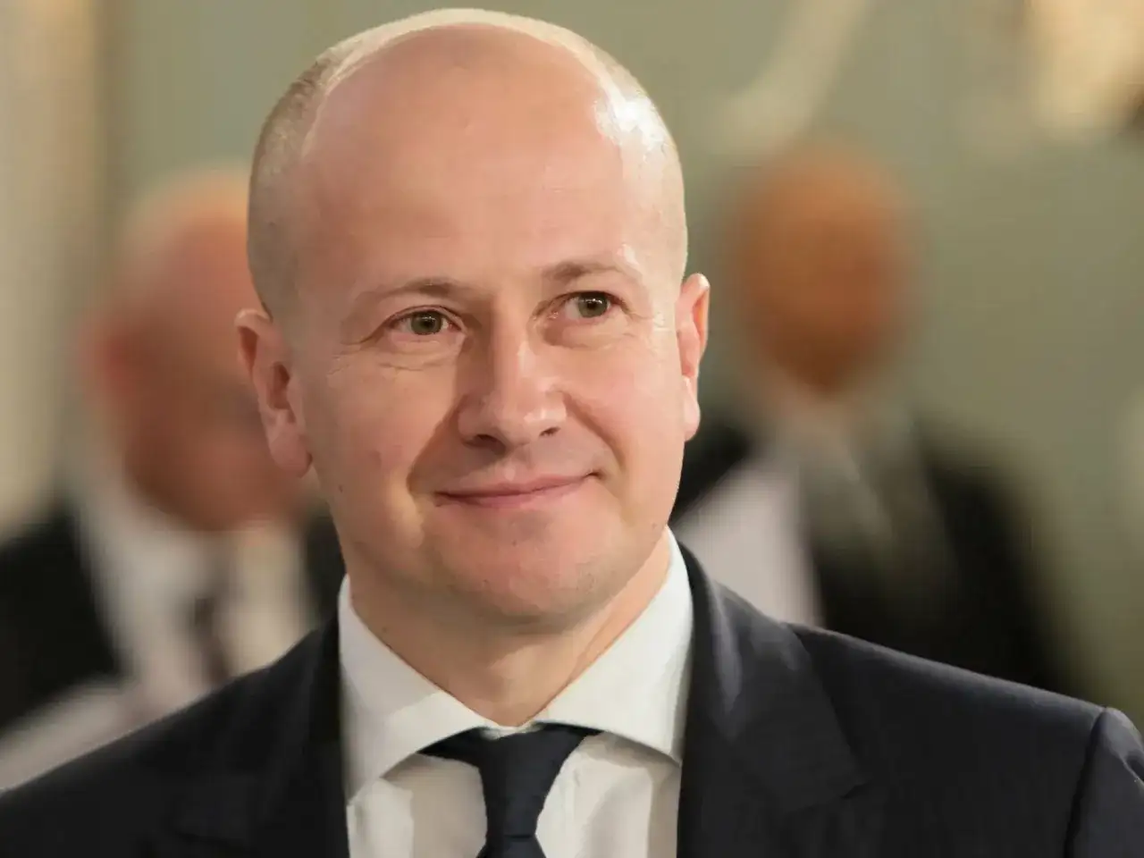 Uśmiechnięty mężczyzna w garniturze, być może partner popularnej aktorki, który zrezygnował z kariery dla niej.