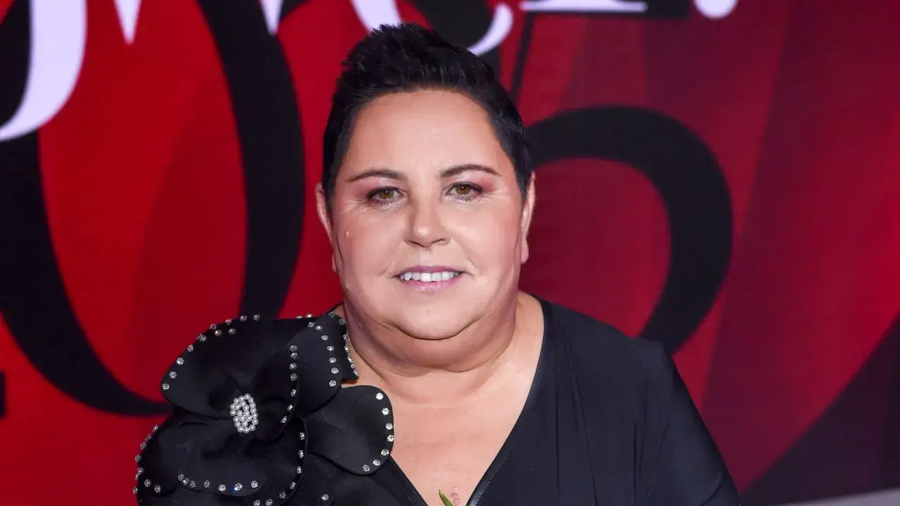 Dorota Wellman w czarnej sukni z ozdobnym kwiatem na ramieniu, z uśmiechem na twarzy.