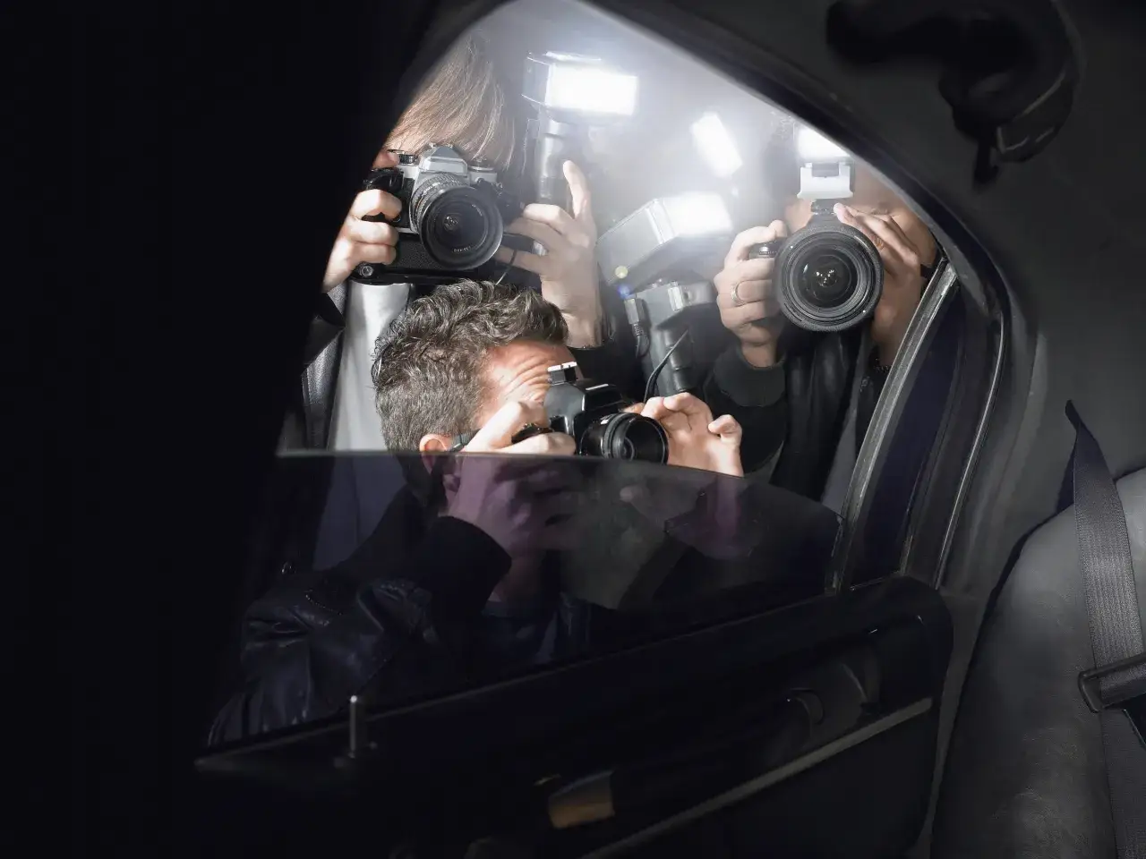 Paparazzi z aparatami i fleszami próbują sfotografować kogoś w samochodzie. To pokazuje, dlaczego polskie gwiazdy ukrywają twarze swoich partnerów w mediach.