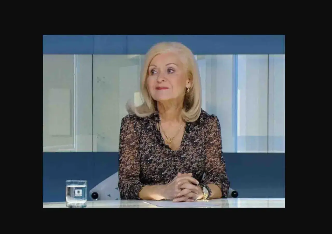 Kobieta z blond włosami, w kwiecistej bluzce, siedzi przy stole. W szklance woda. Ile lat ma Krystyna Hołc?