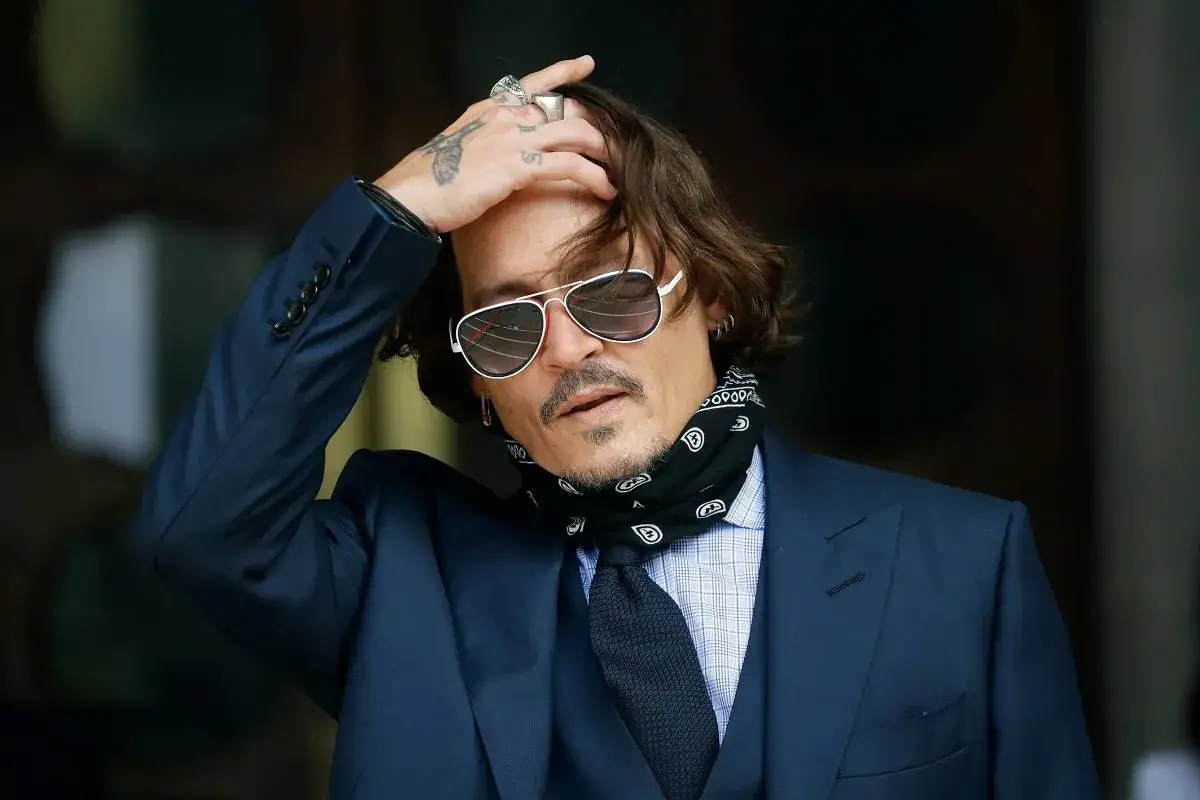 Johnny Depp w garniturze, z ręką na głowie, w okularach przeciwsłonecznych. Jego wizerunek przypomina o najgłośniejszych procesach o zniesławienie między celebrytami w Polsce.