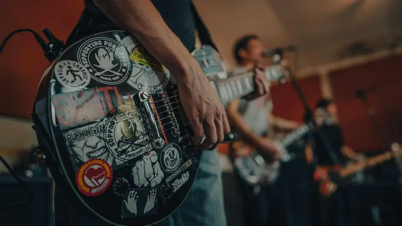 Gitara z naklejkami punkowymi, ręka grającego. Czy to ostatnia trasa zespołu i dlaczego popularny zespół muzyczny nagle zawiesił działalność?