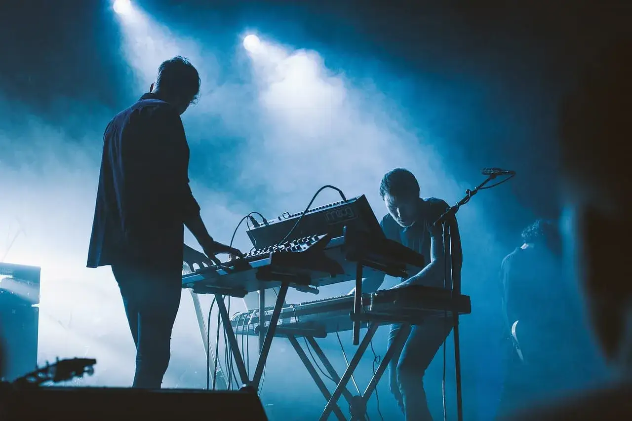 Muzycy grający na syntezatorach na scenie w niebieskim świetle. Czy to ostatni koncert, zastanawiamy się, dlaczego popularny zespół muzyczny nagle zawiesił działalność po trasie.