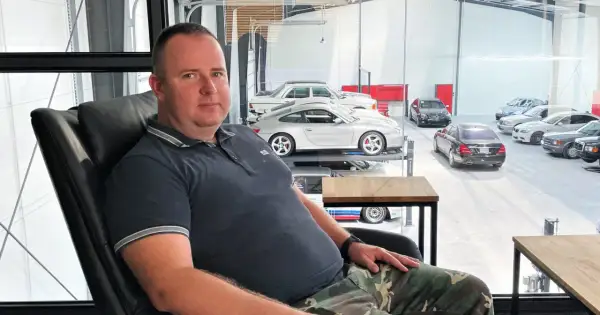 Robert Michalski, w wieku około 40-50 lat, siedzi w czarnym fotelu. W tle widać kolekcję samochodów.