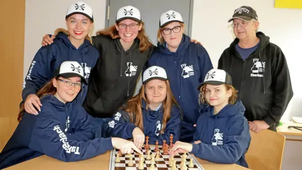 Grupa osób w bluzach i czapkach z logo "TuRa Chess" gra w szachy.