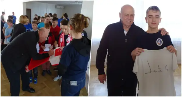 Starszy mężczyzna podpisuje koszulkę dla grupy dzieci, a potem pozuje z młodym chłopcem trzymającym podpisaną koszulkę.